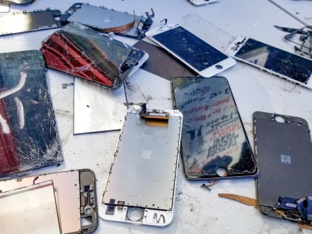 Close-up of a large number of broken cellphones, including cracked cellphone screens with exposed wiring.