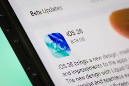 A smartphone screen shows the Apple iOS 26 update with a user's finger preparing to install it. (Photo illustration by Cheng Xin/Getty Images)