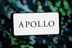 The logo of Apollo Global Management is displayed on a smartphone in front of abstract background. (Photo Illustration by Timon Schneider/Getty Images)